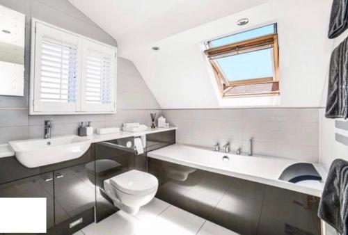 La salle de bains blanche est pourvue de toilettes, d'un lavabo et d'une fenêtre. dans l'établissement Empress Tree Cottage with large hot tub, à Poole