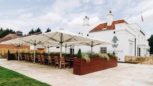 a patio with tables and umbrellas in front of a building at The Wellington Arms - Basingstoke-Reading in Heckfield