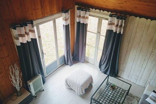 Cette chambre comprend 2 fenêtres avec des rideaux et une table. dans l'établissement Chalet en forêt, brame du cerf, à Valpuiseaux