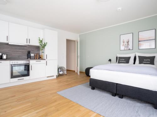 a white bedroom with a large bed and a kitchen at Limehome Dresden Wallstraße - Digital Access in Dresden