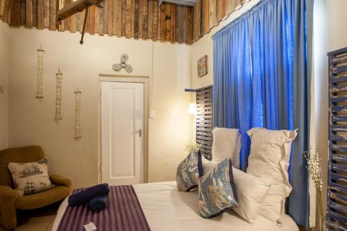 a bedroom with a bed with blue curtains and a chair at Strand Family studio en-suite 6 sleeper Kitchenette Helderberg CT in Cape Town