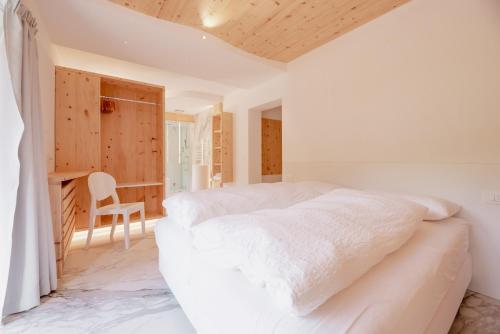 a white bedroom with a bed and a chair at Garnì Aurora Bed and Breakfast in Soraga