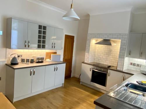 uma cozinha com armários brancos e um forno com placa de fogão em Riverside Cottage em Whalley