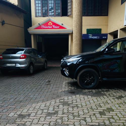 two cars parked in front of a building at Hotel Meridian Palace in Kannur