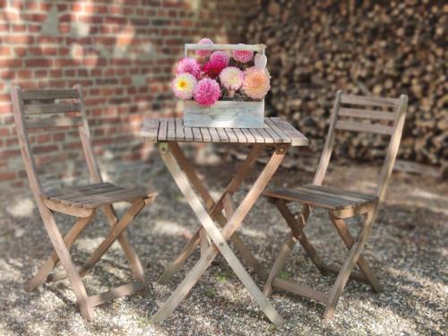 une table avec un vase de fleurs et 2 chaises dans l'établissement Uw eigen boerderij bij Le Moulin de la Place, à Hargicourt