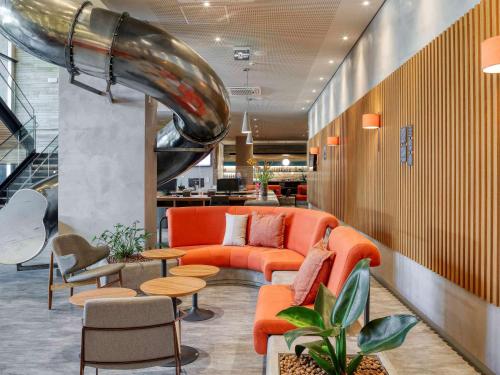 a lobby with an orange couch and tables and chairs at Novotel BH Savassi in Belo Horizonte