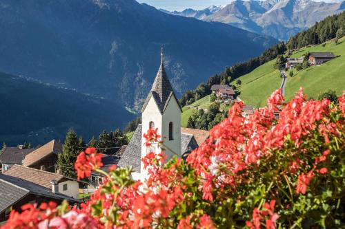 a church in the mountains with red flowers at Tonigbauernhof Enzian in Schenna