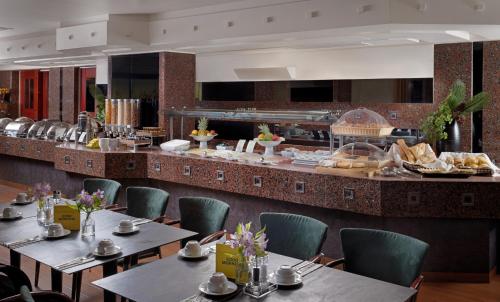 a restaurant with tables and chairs and a buffet at Holiday Inn Athens Attica Av, Airport W., an IHG Hotel in Athens