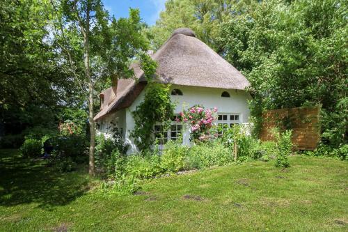a thatch roof house with flowers in the yard at Das alte Zollhaus in Schülp