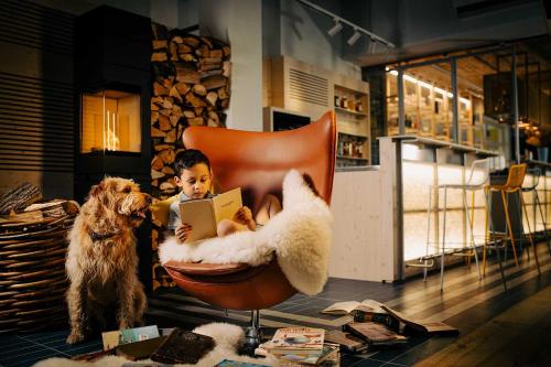 a child sitting in a chair reading a book with two dogs at Gartenhotel Fettehenne in Erkrath