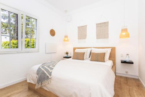 a white bedroom with a large bed and windows at CASA AROEIRA - Beach bungalow near Lisbon in Charneca