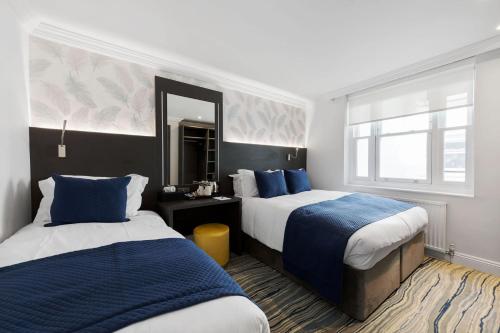 a hotel room with two beds and a mirror at Commodore Hotel in London