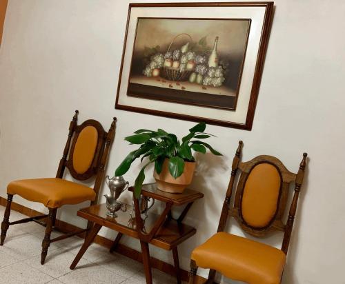 a painting hanging on a wall with two chairs and a plant at Casa Grande in Medellín