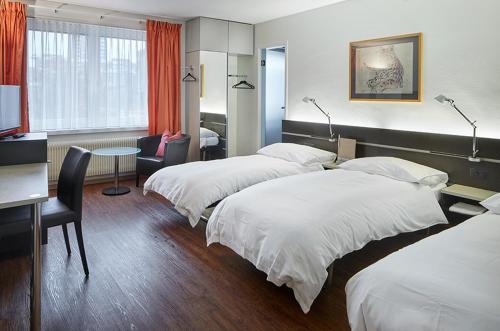 バーゼルにあるホテル デュ コメルスのベッド3台とデスクが備わるホテルルームです。