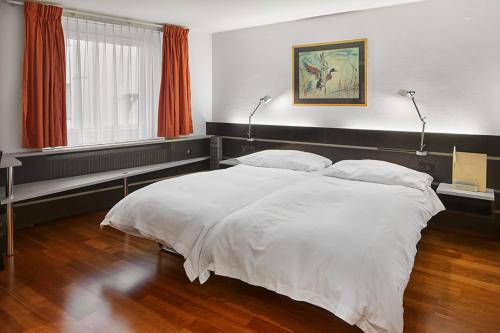 a bedroom with a large white bed with two lamps at Hotel du Commerce in Basel
