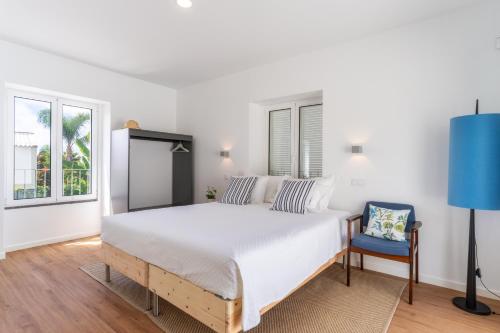 a white bedroom with a large bed and a blue chair at Casa Amarela Apartments - by Casas na Ilha in Câmara de Lobos
