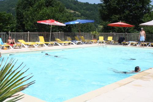 eine Person, die in einem Pool mit Stühlen und Sonnenschirmen schwimmt in der Unterkunft Village de Gite - La Cascade in Sainte-Eulalie-dʼOlt