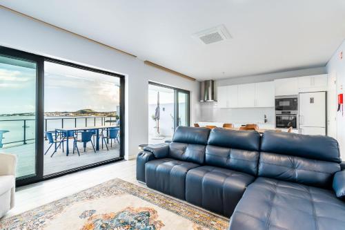 a living room with a leather couch and a kitchen at Facing Bay Hostel in Praia da Vitória