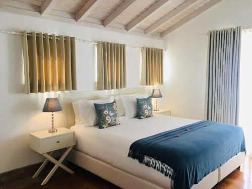 - une chambre dotée d'un grand lit blanc avec des draps et des oreillers bleus dans l'établissement Guarda Rios, à Vila Nova de Milfontes