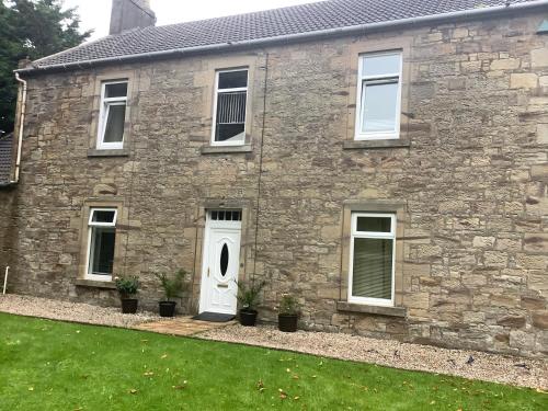 a stone house with a white door and a yard at Nethermains House in Kilwinning