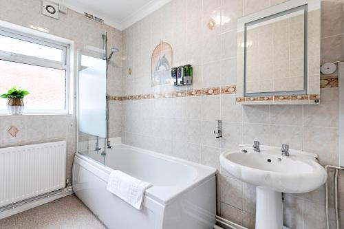 Baño blanco con lavabo, bañera y espejo en Crymlyn Accommodation - TV in Every Bedroom! en Swansea