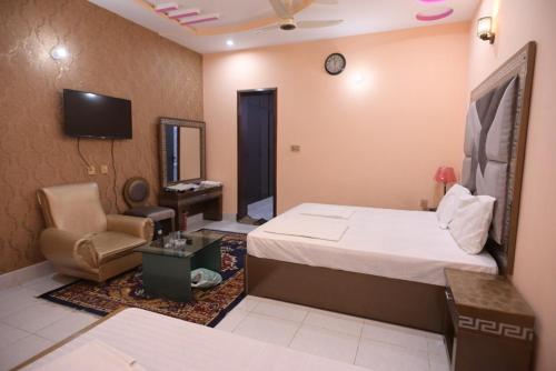 a bedroom with a bed and a chair and a tv at Hotel Shaheen Continental Multan in Multan