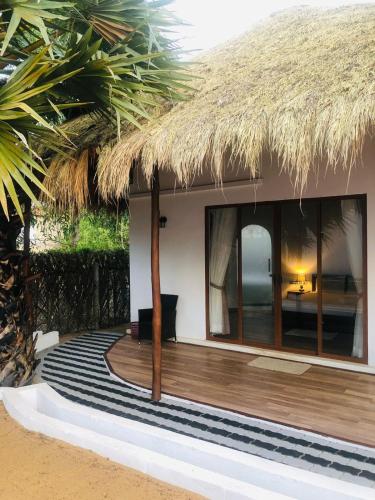 a house with a thatched roof with a wooden deck at The Blue Lagoon Resort Kalpitiya in Kalpitiya