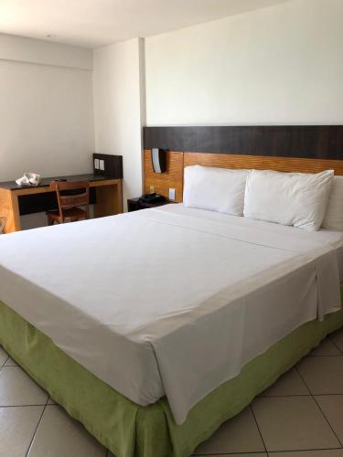 Cette chambre comprend un grand lit blanc et un bureau. dans l'établissement FLAT NATAL PLAZA, à Natal