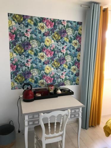 a table and a chair in front of a floral wall at Chambre d'hôte La Clef du Bonheur in Longuenesse