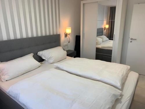 1 dormitorio con 2 camas blancas y espejo en Ferienwohnung in Dornumersiel an der Nordsee, en Dornumersiel