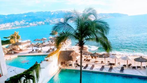 a view of a resort with a palm tree and the ocean at Suite en torres gemelas vista al mar in Acapulco