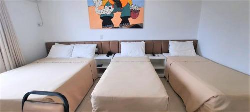 three beds in a room with a painting on the wall at Simas Praia Hotel in Aracaju