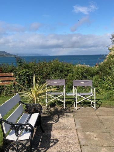two chairs and a bench with the ocean in the background at Ballygally Seaview and Garden Hideaway in Ballygalley