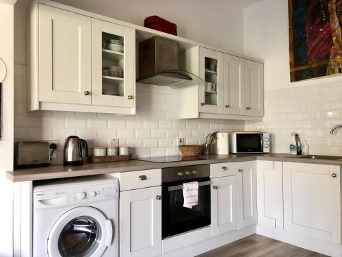 a kitchen with white cabinets and a washing machine at Ballygally Seaview and Garden Hideaway in Ballygalley