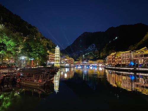 a river with boats in a city at night at Hemu House in Fenghuang