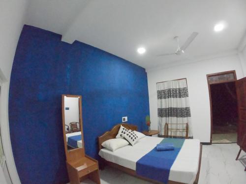 a bedroom with a blue wall with a bed and a mirror at Villa Girilena in Hikkaduwa