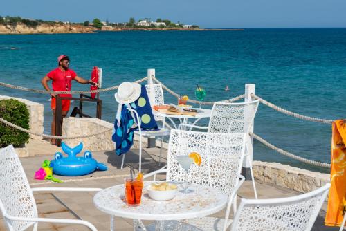 a man standing on the beach with a table and chairs at Hotel President Sea Palace in Noto Marina