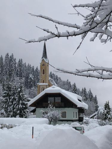 a church with a clock tower covered in snow at Gästehaus Rader in Weissbriach