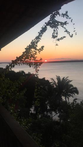 a sunset over the ocean with a palm tree at Pousada Residence Vila das Flores in Morro de São Paulo