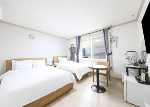 a bedroom with two beds and a table and a window at Mj Hotel in Yeosu