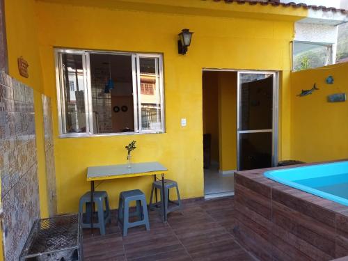 a yellow house with a table and stools and a swimming pool at Cantinho Feliz de Muriqui / Casa amarela in Mangaratiba