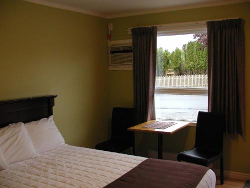 a bedroom with a bed and a desk and a window at Almo Court Motel in Cranbrook