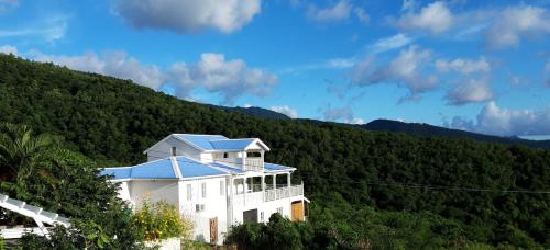 un bâtiment blanc avec un toit bleu sur une montagne dans l'établissement Côté Caraïbes, à Bouillante