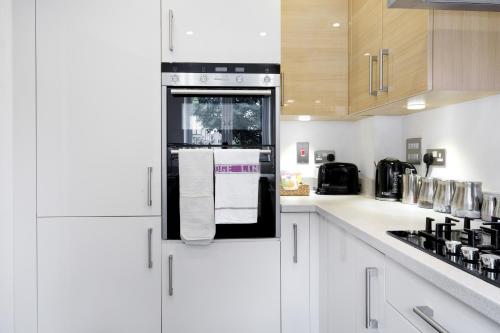 a kitchen with white cabinets and a black refrigerator at London Heathrow Living Holywell Serviced Houses - 3 and 4 bedrooms By Ferndale in Stanwell