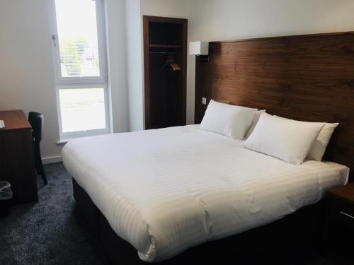 a bedroom with a large white bed with a wooden headboard at Cairn Hotel in Bathgate