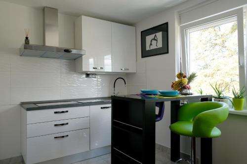 a kitchen with white cabinets and a green stool at Apartman MIMA in Karlovac