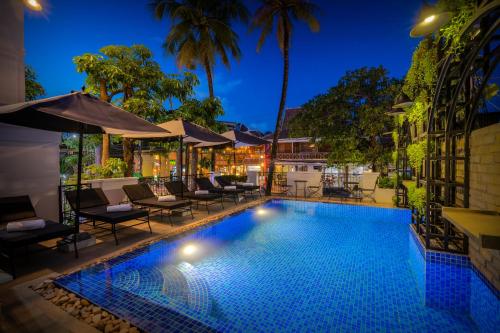 uma piscina à noite com cadeiras e guarda-sóis em Blanc Smith Residence em Siem Reap