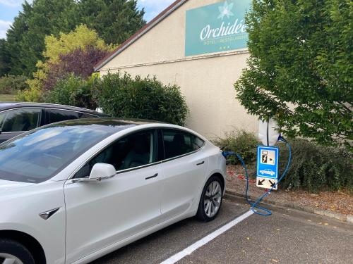 a white car is plugged into a electric car charger at Les Orchidées , Hôtel & Restaurant in Verdun