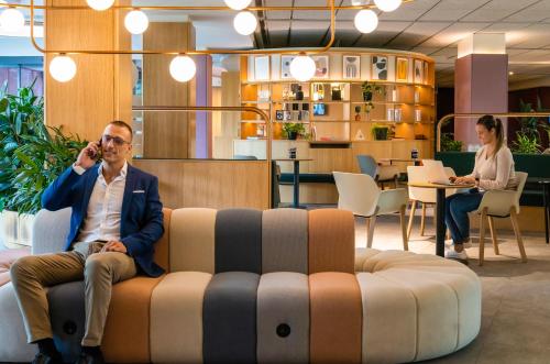 a man sitting on a couch talking on a cell phone at Ibis Styles Madrid City Las Ventas in Madrid
