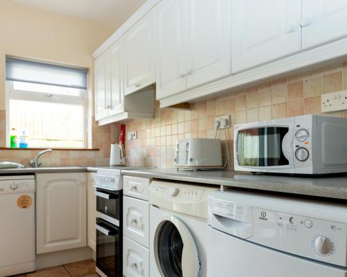 uma cozinha com electrodomésticos brancos e armários brancos em Dartry Close em Bundoran